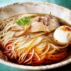 Pyszny, domowy ramen z makaronem, plastrami mięsa, bambusem i jajkiem na twardo, posypany szczypiorkiem i papryką.