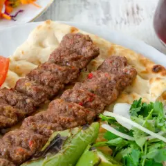 Pyszny Adana kebab przepis na talerzu z pitą, pomidorem, papryką i sałatką. Idealny na letni obiad.