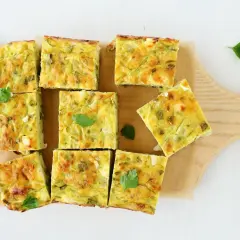 Pyszna frittata z cukinią pokrojona w kwadraty, ułożona na desce.