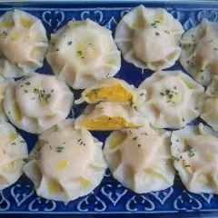 Pyszne pierogi z dynią, polane masłem i posypane szczypiorkiem, ułożone na niebieskiej paterze.