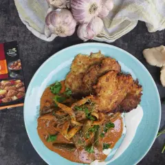 Pyszny gulasz z boczniaka na talerzu z plackami ziemniaczanymi i śmietaną. Obok świeże boczniaki i przyprawa do gulaszu.