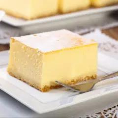 Pyszny kawałek new york cheesecake, oprószony cukrem pudrem, czeka na widelcu na talerzyku.