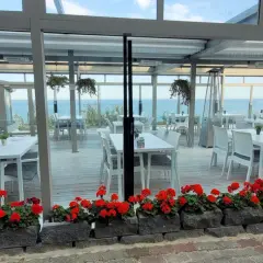 Letnia atmosfera przy plaży w Hotelu Lambert. Stoliki i krzesła czekają na gości, a morze w tle zaprasza do relaksu.