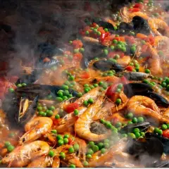 Pyszne hiszpańskie jedzenie: paella z krewetkami, małżami, groszkiem i pomidorami, parująca w wielkiej patelni.