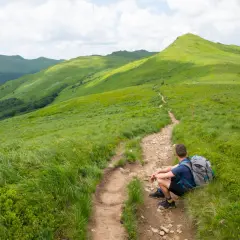 Turysta odpoczywa na szlaku, podziwiając zielone połoniny. Bieszczady atrakcje to piękne widoki i aktywne spędzanie czasu.