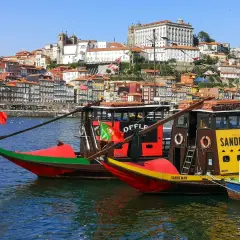 Porto na weekend: tradycyjne łodzie Rabelo na rzece Douro, z kolorowymi domami i zabytkowymi budynkami w tle.
