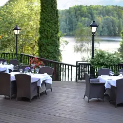 Elegancki taras z widokiem na jezioro, idealne miejsce na relaks w spa Mazury. Stoły nakryte do kolacji, otoczone zielenią.