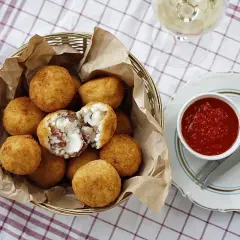 Koszyk pełen złotych arancini, jedno przekrojone ukazuje ryż i ser. Obok miseczka z sosem pomidorowym. Idealne na przekąskę, gdy masz ochotę na arancini przepis.