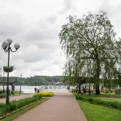 Spacer w Mrągowie nad jeziorem, z wierzbą płaczącą i kwitnącymi rabatami. Idealne miejsce na relaks i podziwianie mrągowskich atrakcji.