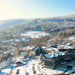 Malowniczy hotel ze stokiem w zimowej scenerii. Śnieg pokrywa dachy domów i drzewa, tworząc bajkowy krajobraz.