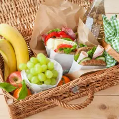 Koszyk piknikowy pełen smakołyków: kanapki, winogrona, banany, jabłko i mandarynka. Idealne co na piknik!