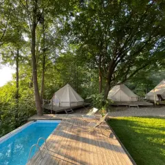 Luksusowy glamping nad jeziorem: namioty tipi na drewnianych tarasach, basen i leżaki wśród drzew. Idealne miejsce na relaks.