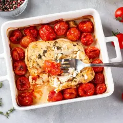 Pyszna feta zapiekana z pomidorkami koktajlowymi, czosnkiem i ziołami. Widok z góry na danie w naczyniu żaroodpornym.