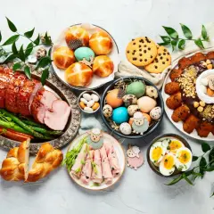 Wielkanocny stół z pieczonym mięsem, babkami, jajkami, ciastkami i dekoracjami.