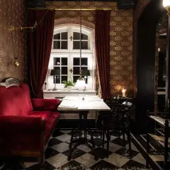 Eleganckie wnętrze z czerwoną kanapą i marmurowym stołem, przypominające pałac w Ciekocinku. Wzory na tapecie i czarno-biała szachownica na podłodze tworzą wyjątkowy klimat.