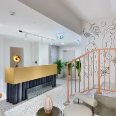 Nowoczesne wnętrze kliniki La Perla SPA w Nałęczowie. Złota recepcja, schody z brzoskwiniową balustradą i artystyczne rysunki na ścianie tworzą elegancką atmosferę.