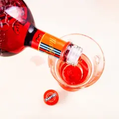 Czerwony Martini Fiero Tonic nalewany do szklanki. Obok leży czerwona zakrętka z logo Martini.
