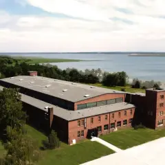 Dawny kompleks przemysłowy, dziś arche Mielno, z ceglanymi budynkami i wieżą, nad jeziorem.
