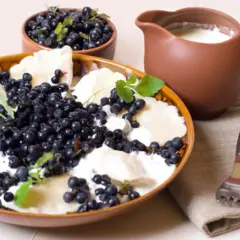 Pierogi z jagodami i śmietaną, miseczka owoców i dzbanek mleka. Idealny comfort food na letni dzień.