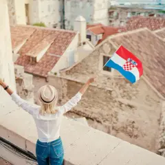 Kobieta z chorwacką flagą na tle dachów. Pozwala to na naukę podstawowych zwrotów po chorwacku.
