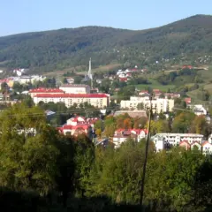 Widok na Ustrzyki Dolne z górami w tle. Miasto z czerwonymi dachami i nowoczesnymi budynkami, otoczone zielenią. Atrakcje turystyczne czekają!