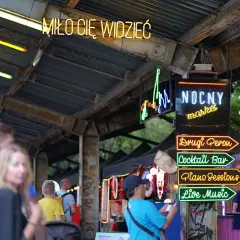Nocny market Warszawa wita neonami: "Miło Cię Widzieć", "Drugi Peron", "Cocktail Bar", "Piano Sessions", "Live Music".