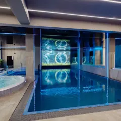 Nowoczesny basen i jacuzzi w rezydencji Aqua Szklarska Poręba. Niebieskie podświetlenie i ekran z animacją tworzą relaksującą atmosferę.