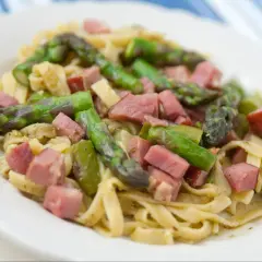 Pyszne spaghetti ze szparagami i kawałkami szynki na białym talerzu.