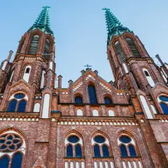Dwie wieże ceglanego kościoła z zielonymi iglicami, jeden z najpiękniejszych kościołów w Polsce, pod błękitnym niebem.