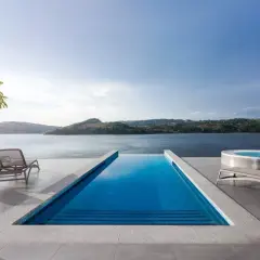 Relaks przy basenie z widokiem na góry i jezioro. Dwa leżaki i jacuzzi czekają na gości.