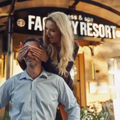 Zaskoczenie przed Factory Resort Kołobrzeg. Kobieta zakrywa oczy mężczyźnie, który uśmiecha się, czekając na niespodziankę.