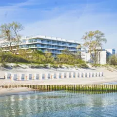 Nowoczesny seaside park hotel z widokiem na plażę i morze. Rząd białych leżaków plażowych czeka na gości.