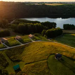 Malownicze domki nad jeziorem, idealne na tani wypad na weekend w Polsce. Złote słońce oświetla zielone pola i lasy.