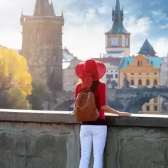 Kobieta w czerwonym kapeluszu podziwia praskie praga nietypowe atrakcje, w tym Most Karola i wieże.