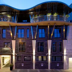 Nowoczesny hotel niebieski z falistym dachem i kamienną fasadą. Wejście oświetlone, obok garaż.