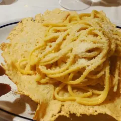 Pyszne spaghetti z parmezanem, podane na chrupiącym serowym "gniazdku". Idealna odpowiedź na pytanie: co zjeść we Włoszech.