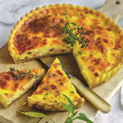Pyszny quiche lorraine z boczkiem i ziołami, pokrojony na desce, z nożem i gałązkami tymianku.