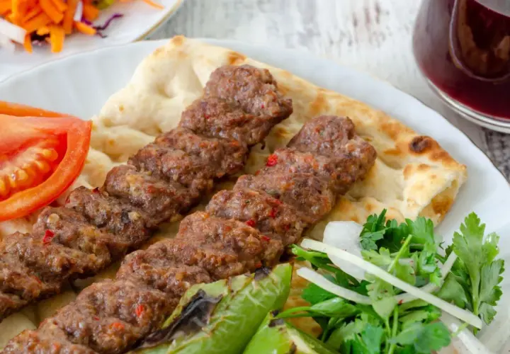 Pyszny Adana kebab przepis na talerzu z pitą, pomidorem, papryką i sałatką. Idealny na letni obiad.