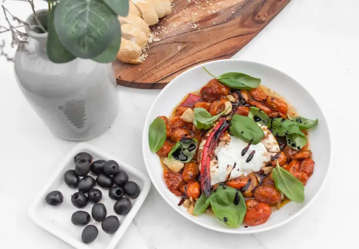 Pyszny burrata przepis: kremowy ser z pieczonymi pomidorkami, czosnkiem, bazylią i oliwkami. Idealny na letni obiad.