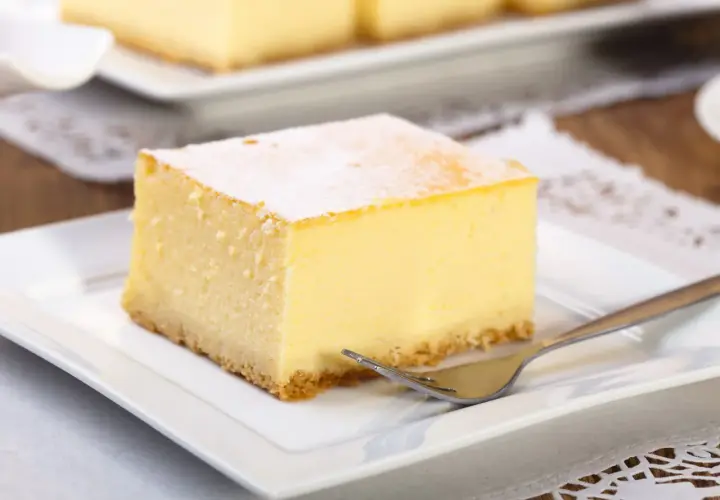 Pyszny kawałek new york cheesecake, oprószony cukrem pudrem, czeka na widelcu na talerzyku.