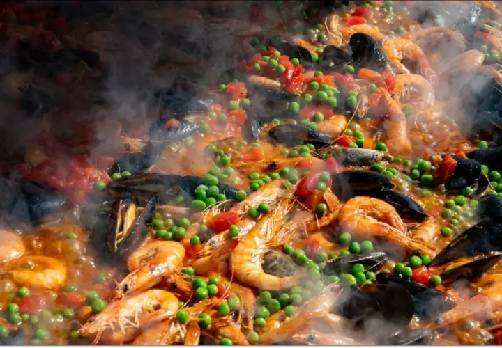 Pyszne hiszpańskie jedzenie: paella z krewetkami, małżami, groszkiem i pomidorami, parująca w wielkiej patelni.