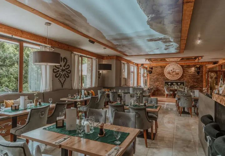 Przytulna restauracja w górach z widokiem na las. Drewniane belki, kamienne detale i sufit z malowniczym krajobrazem tworzą niepowtarzalny klimat.