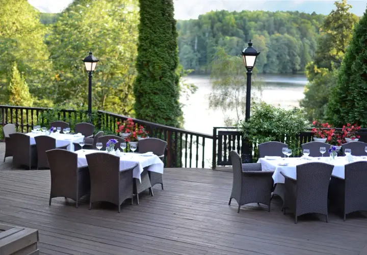 Elegancki taras z widokiem na jezioro, idealne miejsce na relaks w spa Mazury. Stoły nakryte do kolacji, otoczone zielenią.