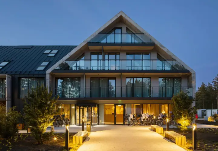 Nowoczesny budynek Saltic Resort & Spa Łeba z betonowymi elementami i przeszklonymi balkonami, oświetlony wieczorem.