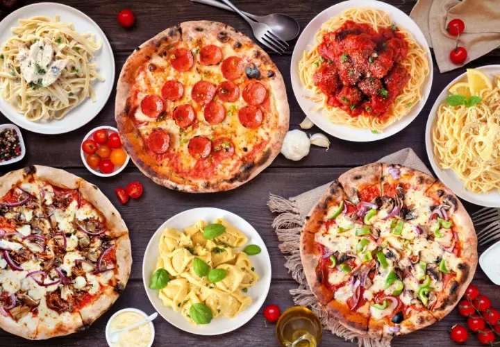 Uczta w stylu kuchnia włoska: pizze, spaghetti z klopsikami, fettuccine i tortellini na drewnianym stole.
