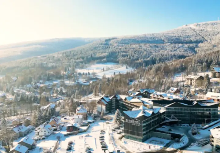 Malowniczy hotel ze stokiem w zimowej scenerii. Śnieg pokrywa dachy domów i drzewa, tworząc bajkowy krajobraz.
