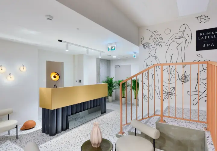 Nowoczesne wnętrze kliniki La Perla SPA w Nałęczowie. Złota recepcja, schody z brzoskwiniową balustradą i artystyczne rysunki na ścianie tworzą elegancką atmosferę.