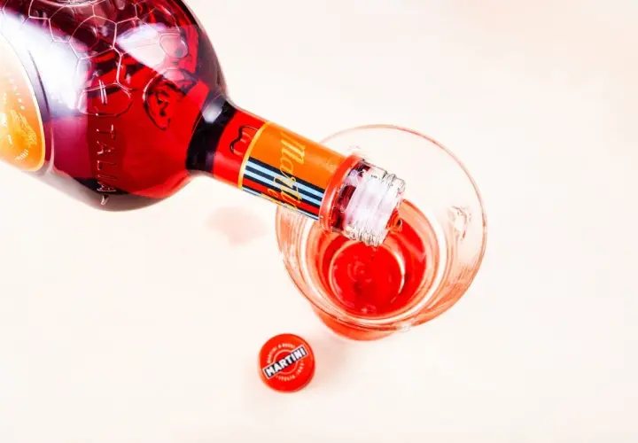 Czerwony Martini Fiero Tonic nalewany do szklanki. Obok leży czerwona zakrętka z logo Martini.