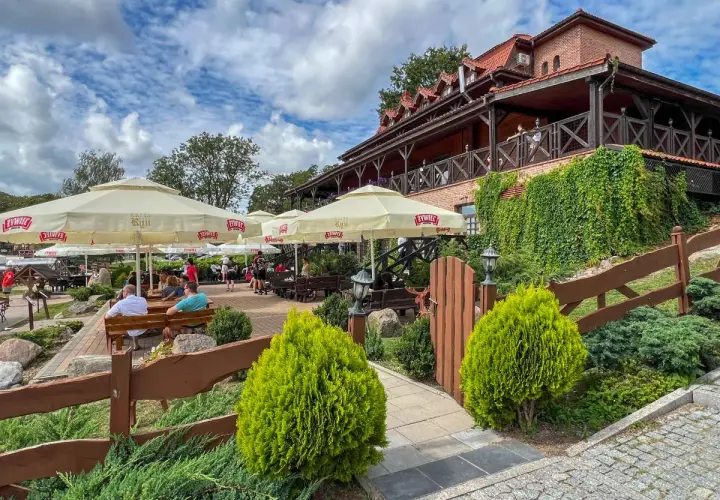 Letnie popołudnie w jednej z najlepszych restauracji na Mazurach. Goście odpoczywają pod parasolami, ciesząc się widokiem na jezioro.