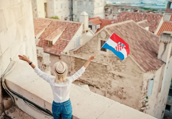 Kobieta z chorwacką flagą na tle dachów. Pozwala to na naukę podstawowych zwrotów po chorwacku.